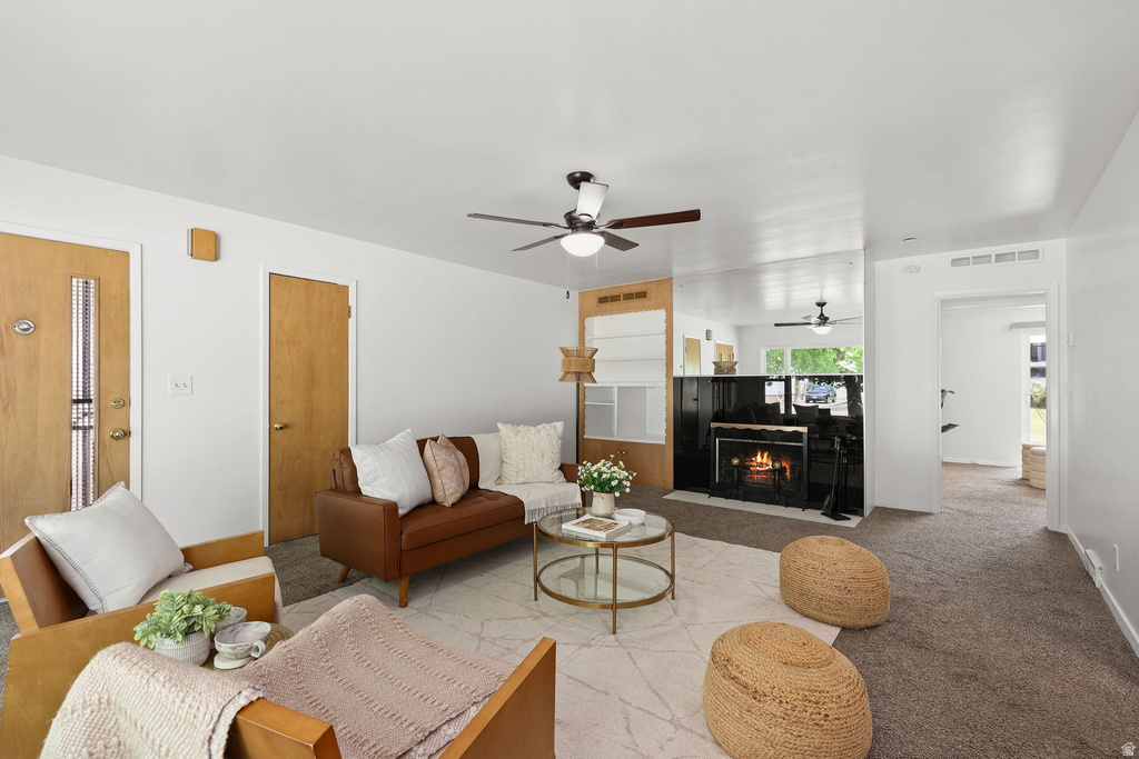Carpeted living area featuring a fireplace with a black surround, a ceiling fan, and light wood-finish doors
