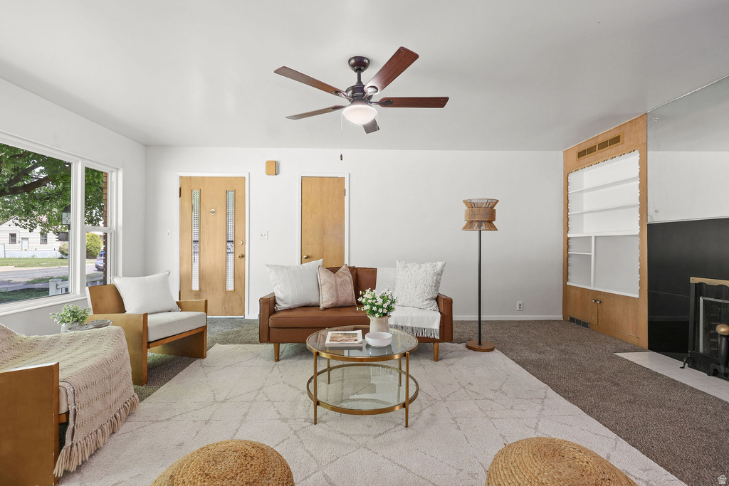 Bright living space featuring a ceiling fan, light wood doors, large windows, an integrated shelving unit, and a fireplace with a black surround