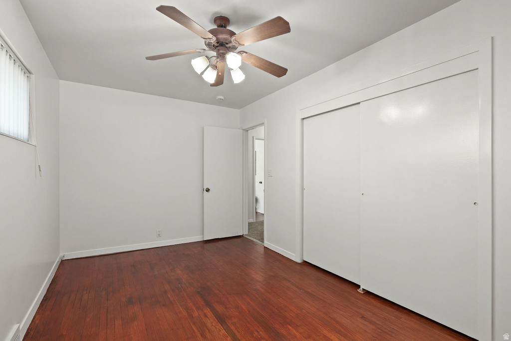 Room featuring wood-finish flooring, a ceiling fan with integrated lighting, a window with vertical blinds, and a built-in sliding door closet