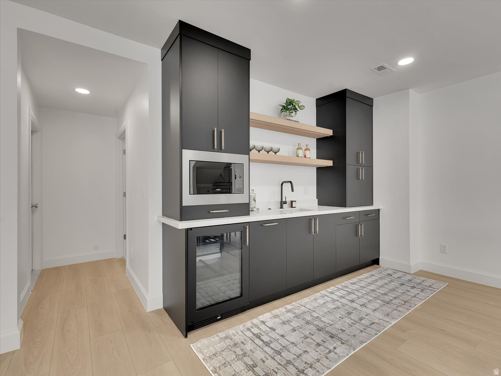 Indoor wet bar with open shelves, wine cooler, light wood-style flooring, recessed lighting, and dark cabinets
