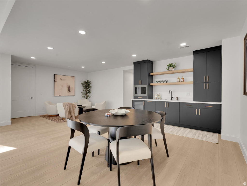 Dining space with light wood-type flooring, recessed lighting, and bar with sink