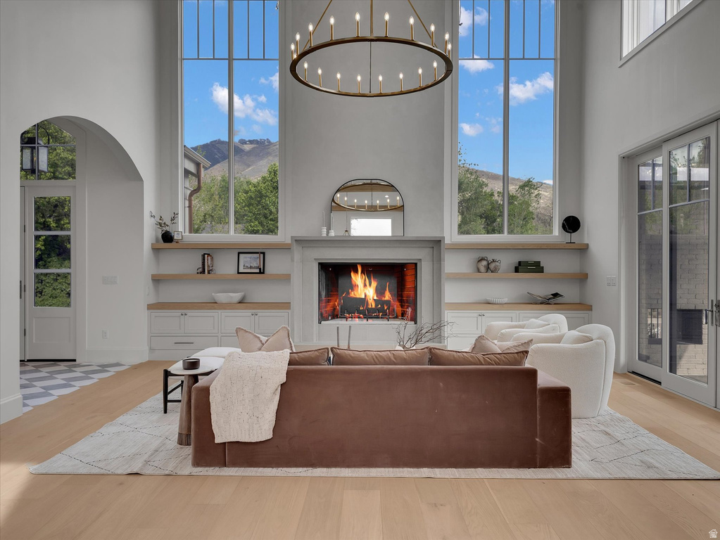 Living room featuring a high ceiling, a lit fireplace, light wood-type flooring, a mountain view, and arched walkways