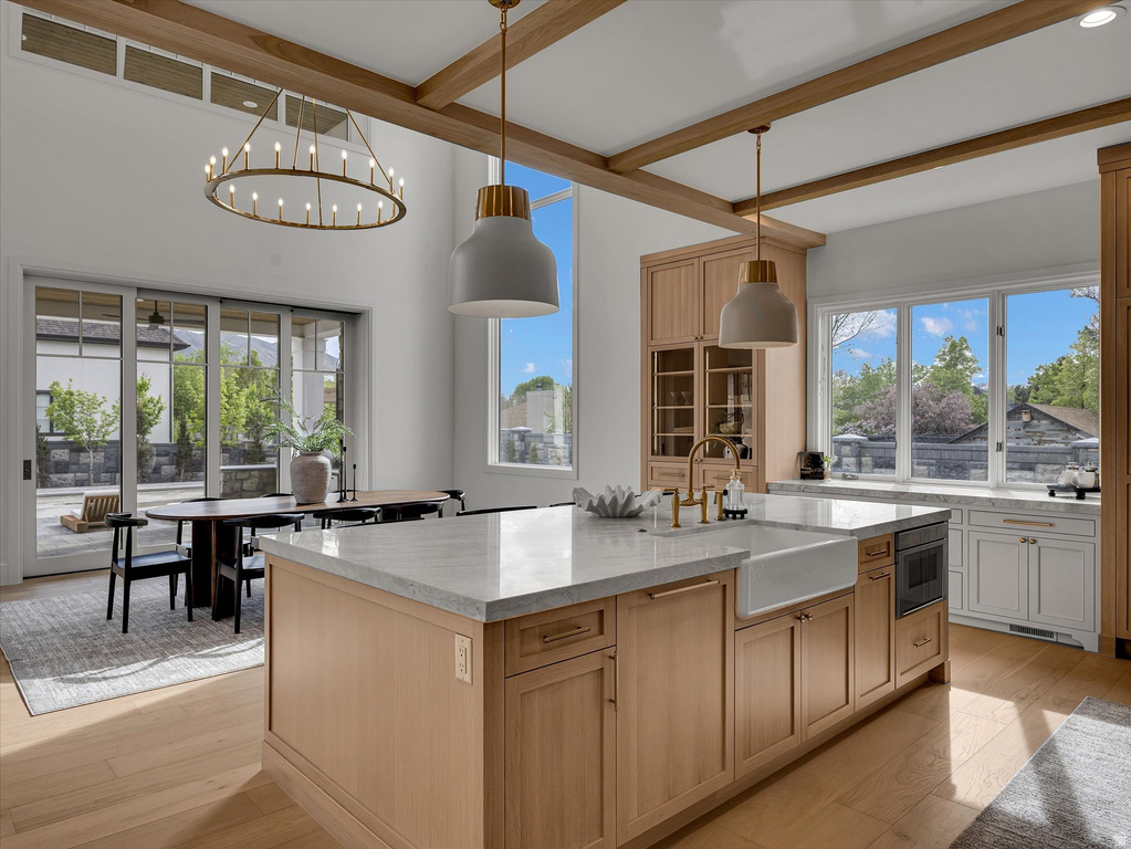 Kitchen featuring light stone countertops, a kitchen island with sink, beamed ceiling, light wood-style floors, and two tone cabinetry