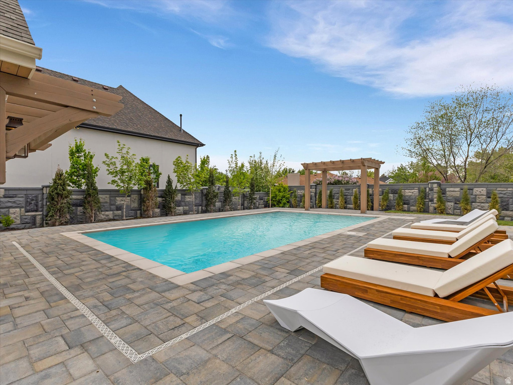 View of pool with a pergola, patio surround, and a fenced backyard