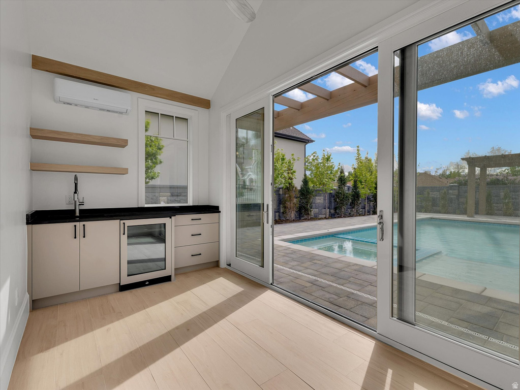 Indoor wet bar featuring dark countertops, beverage cooler, open shelves, plenty of natural light, and vaulted ceiling