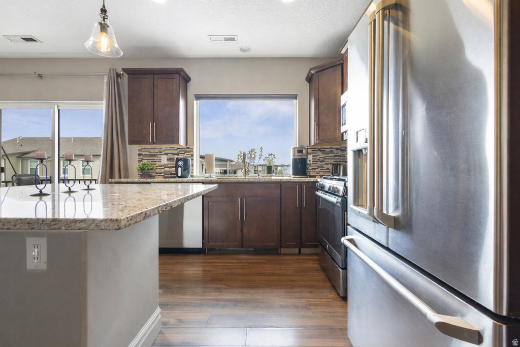 Kitchen with stainless steel appliances, dark wood finish cabinetry, light stone countertops, tasteful backsplash, and a textured ceiling