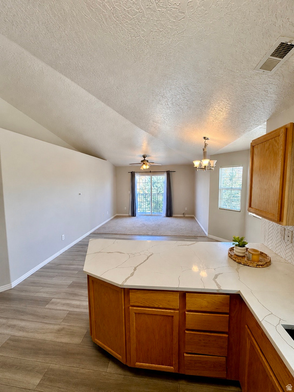 Open-concept living area featuring a kitchen island with a light-toned countertop, wood-finish flooring, a vaulted ceiling, and carpeted living space with a ceiling fan