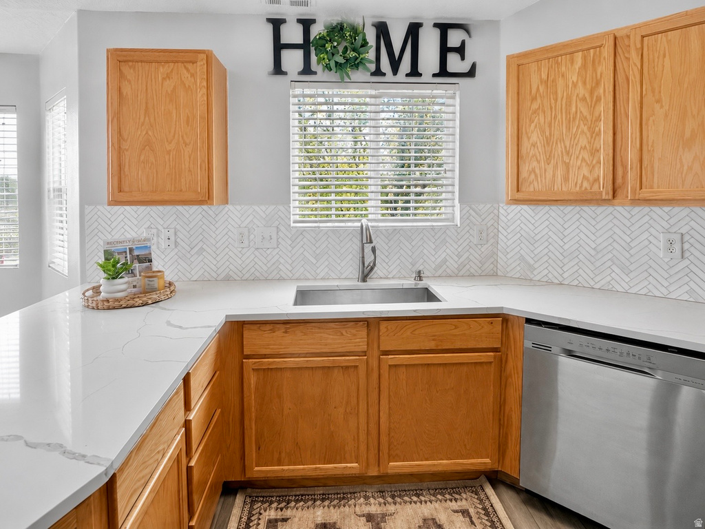 Kitchen featuring abundant wood cabinetry, white countertops, herringbone tile backsplash, an undermount stainless steel sink with a gooseneck faucet, and a stainless steel dishwasher