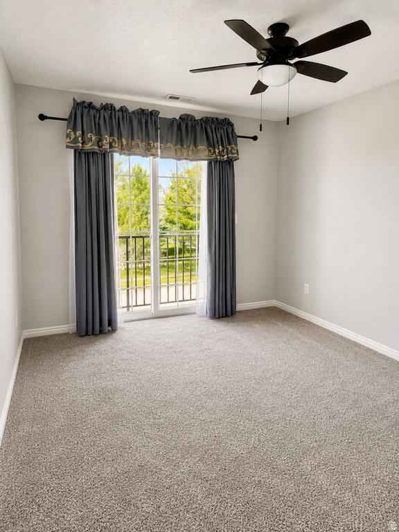 Carpeted room featuring a ceiling fan with integrated lighting, a sliding glass door with a wrought iron balcony, and contemporary light grey wall paint