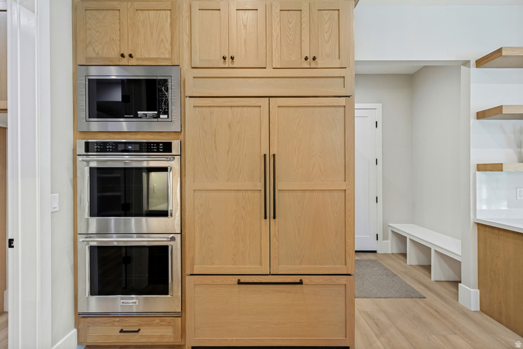 Built-in stainless steel microwave and double ovens integrated into light wood-finish cabinetry