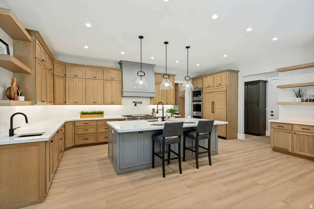Spacious kitchen featuring light wood-finish cabinetry, a large center island with seating, a gray range hood, and integrated appliances