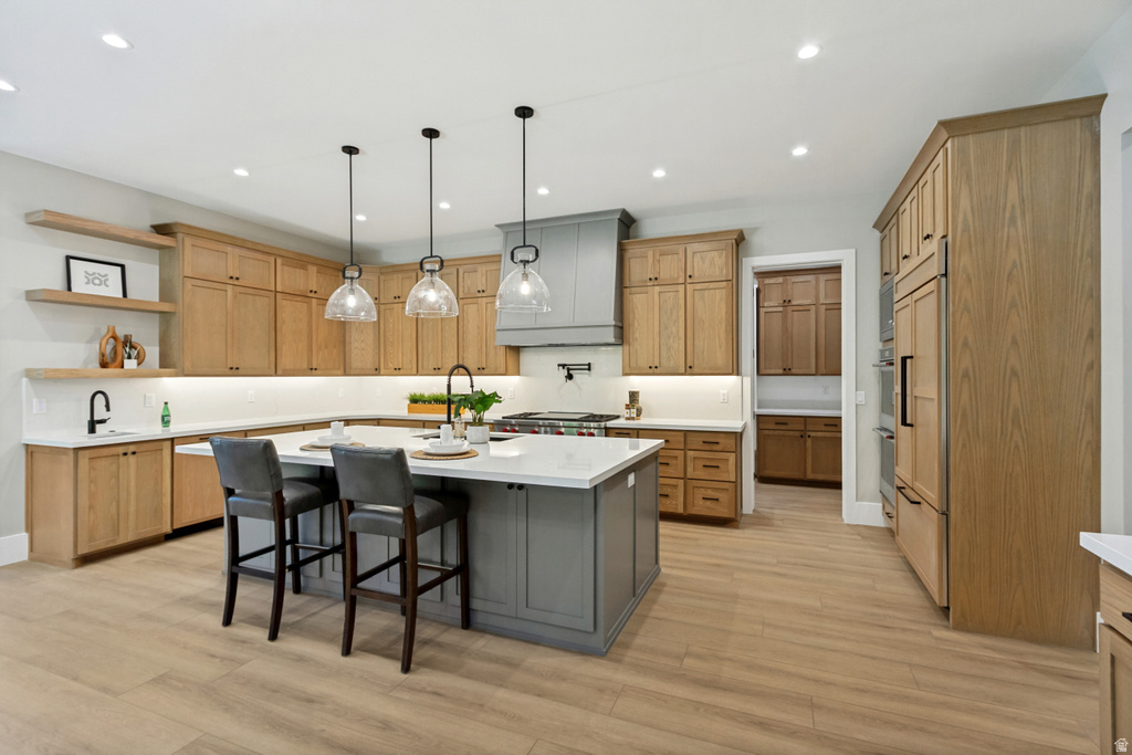 Contemporary kitchen featuring wood-finish cabinetry, a large center island with seating, a custom range hood, and integrated appliances