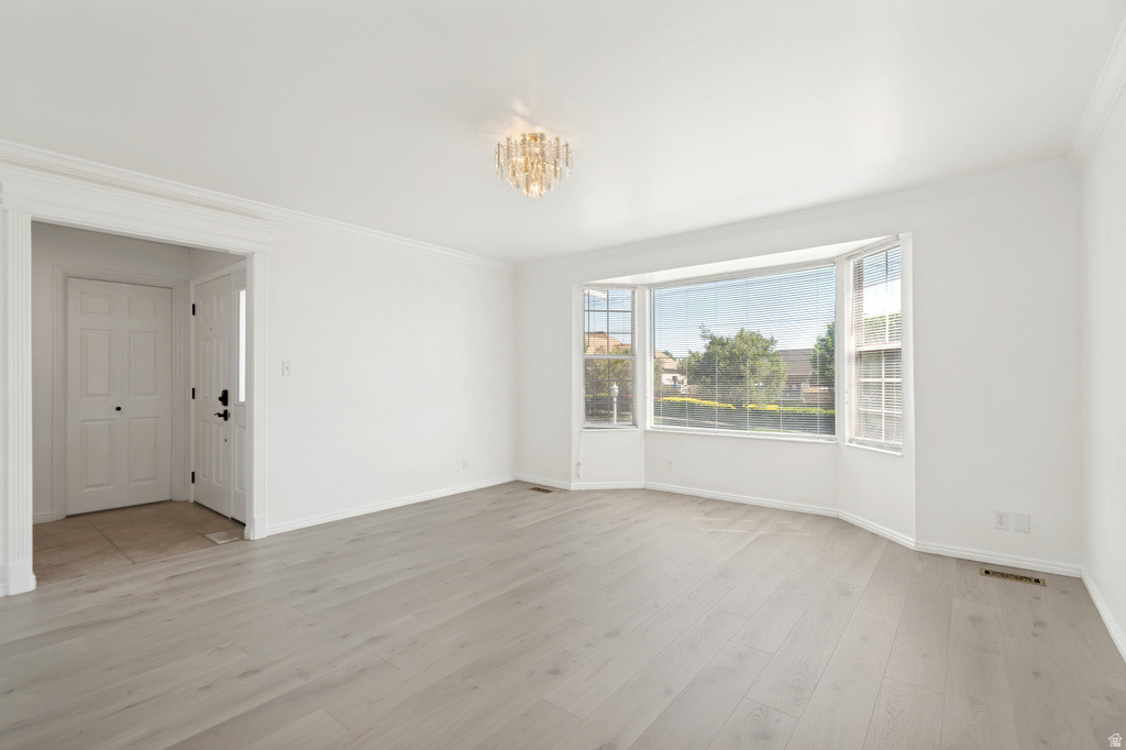 Spacious interior room featuring a prominent bay window, light wood-finish flooring, white walls, and elegant crown molding