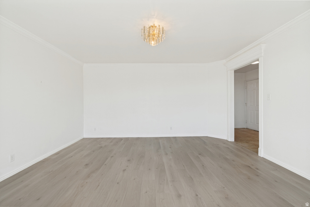 Spacious room featuring light wood-finish flooring, white walls, crown molding, and a decorative ceiling light fixture