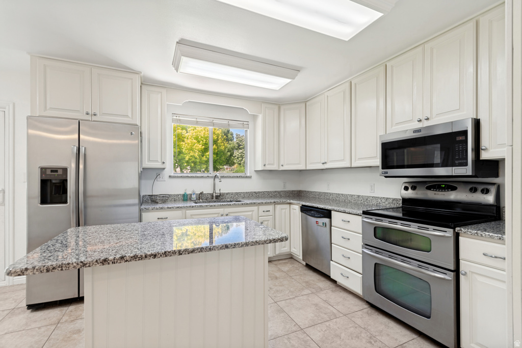 Kitchen featuring white cabinetry, granite countertops, stainless steel appliances, a center island with beadboard paneling, and tile flooring