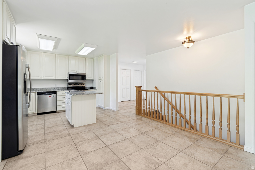 Kitchen featuring white cabinetry, stainless steel appliances, a center island with a granite-style countertop, and neutral tile flooring