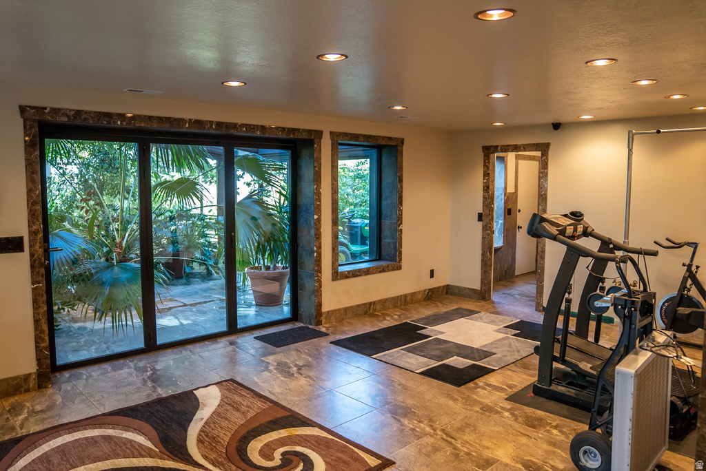 Interior space featuring large format tile flooring, recessed ceiling lighting, and a multi-panel glass door opening to an exterior area with lush foliage