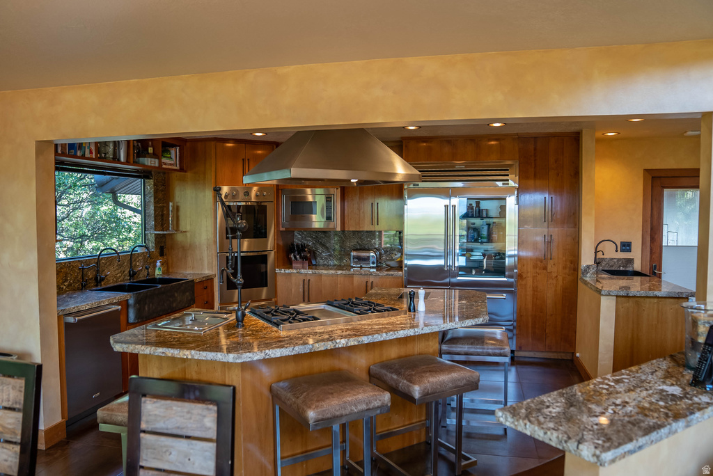 Gourmet kitchen featuring a central island with a built-in gas cooktop, stainless steel appliances, granite countertops, wood cabinetry, and a double basin sink