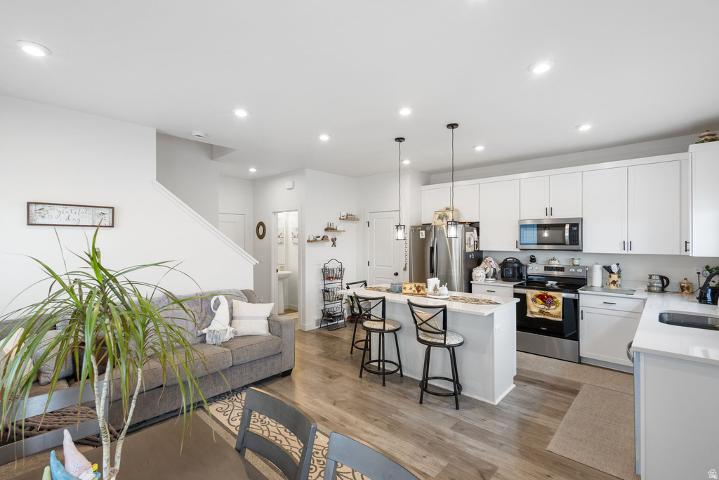 Kitchen featuring stainless steel appliances, light stone counters, a kitchen island, a kitchen bar, and white cabinets