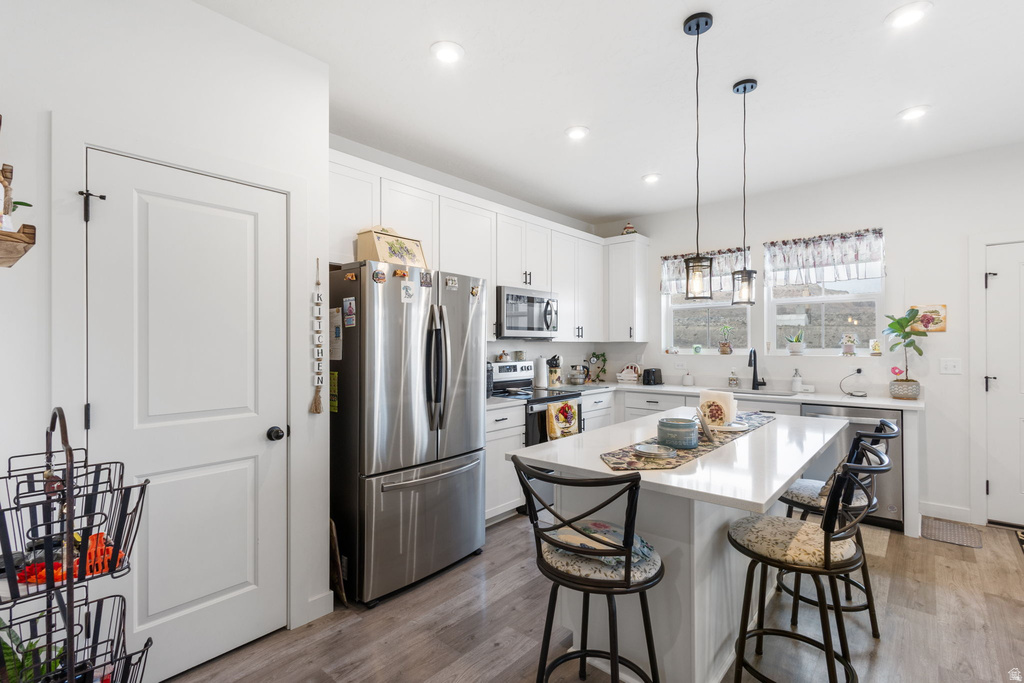 Kitchen with stainless steel appliances, a kitchen bar, decorative light fixtures, a kitchen island, and light wood finished floors