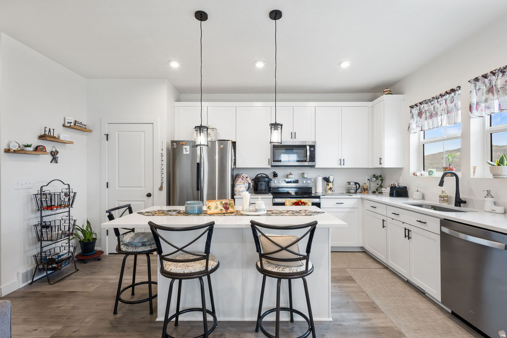 Kitchen featuring white cabinetry, stainless steel appliances, a center island, a kitchen breakfast bar, and pendant lighting