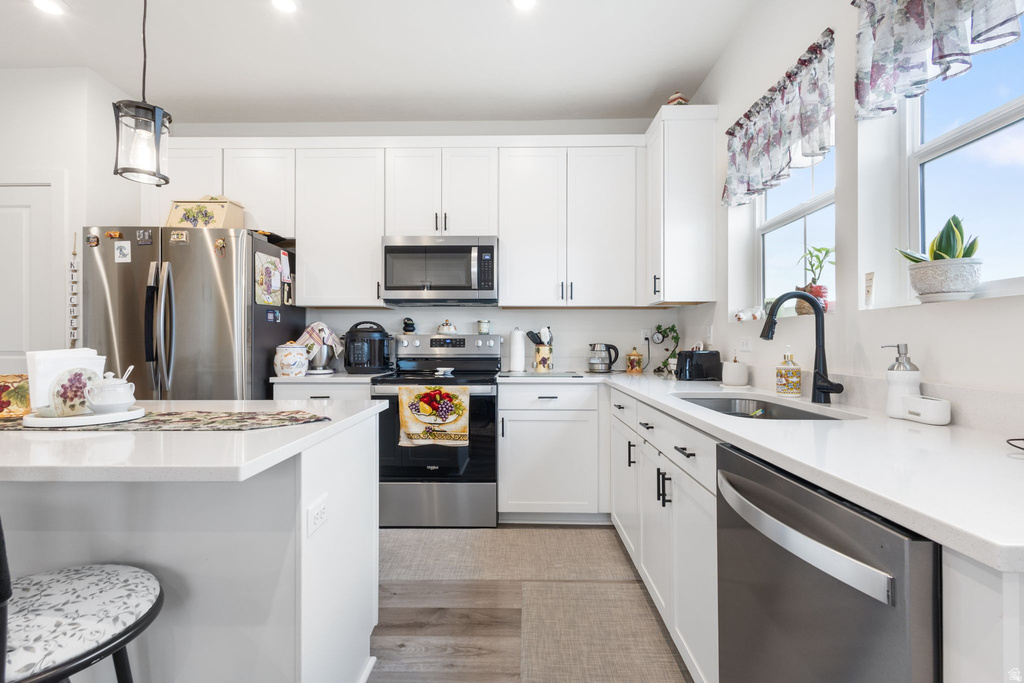 Kitchen featuring white cabinets, stainless steel appliances, hanging light fixtures, light stone countertops, and a breakfast bar