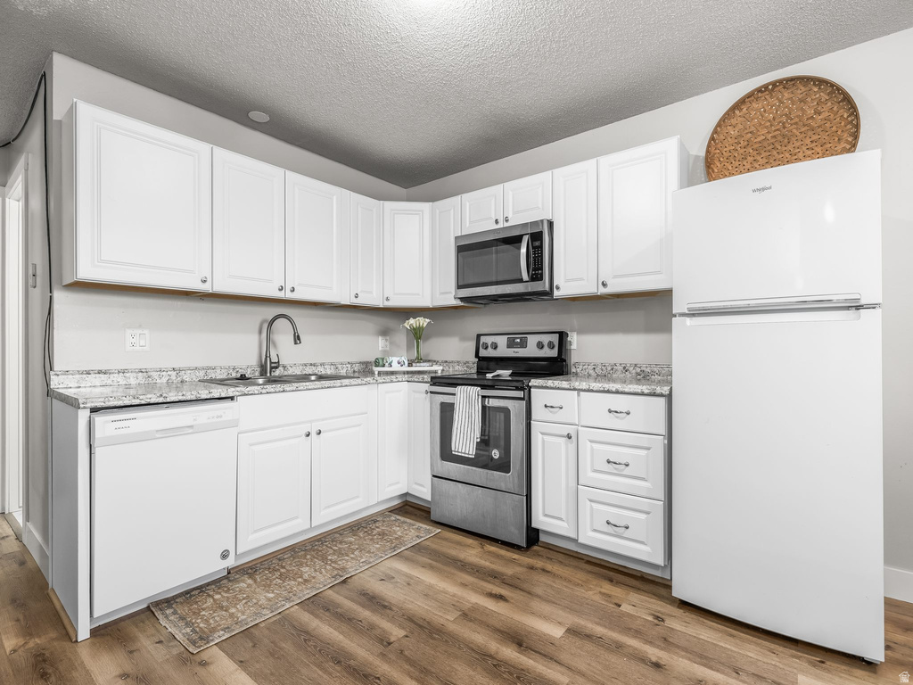 Corner kitchen featuring white cabinetry, light speckled countertops, and wood-finish flooring