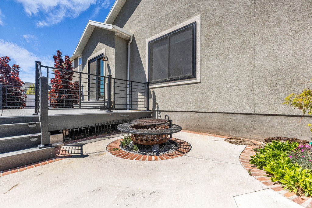 Exterior deck with black metal railings, concrete patio, and a built-in fire pit with a brick border