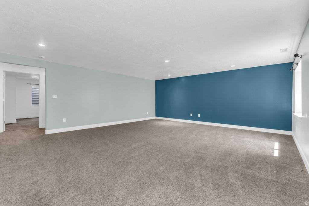 Spacious carpeted room featuring a distinctive accent wall, recessed lighting, and white baseboards