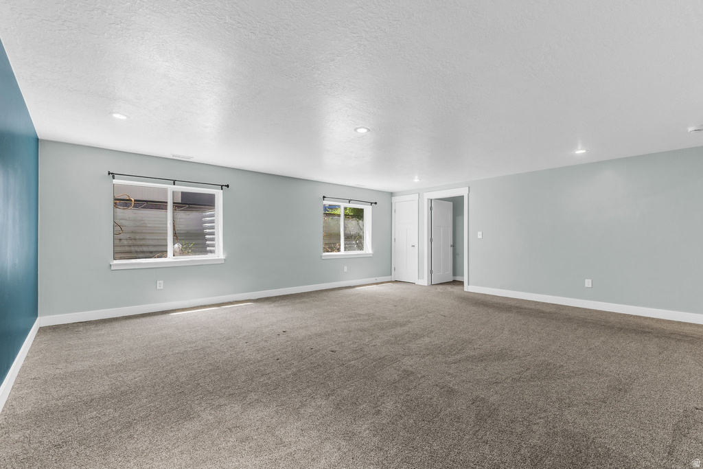Spacious room featuring gray carpeting, light blue painted walls with a dark blue accent wall, two windows with white trim, and white baseboards
