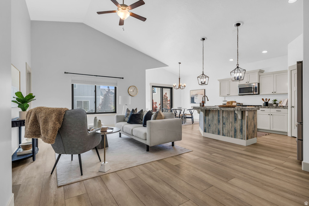 Open concept living area featuring vaulted ceilings, wood-finish flooring, a kitchen island with pendant lighting, and light-toned cabinetry
