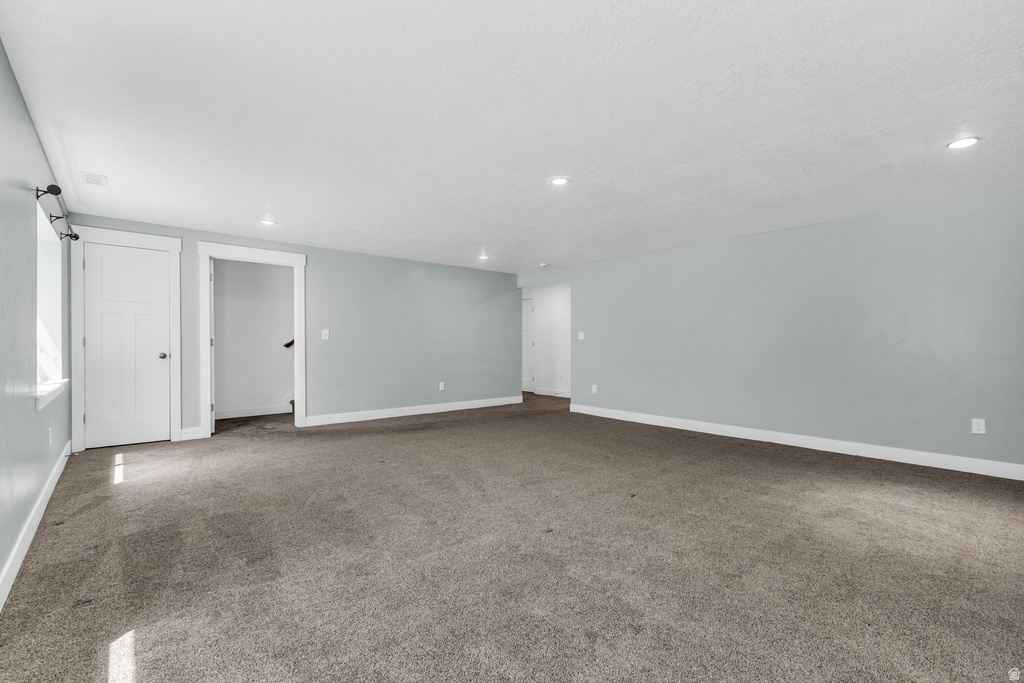 Spacious interior room featuring light blue walls, grey carpeting, recessed lighting, and white baseboards