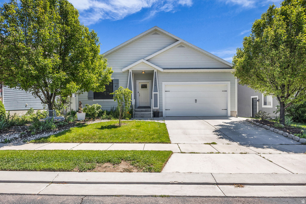 Light-toned siding exterior with a white garage door, covered entry, and established front yard landscaping