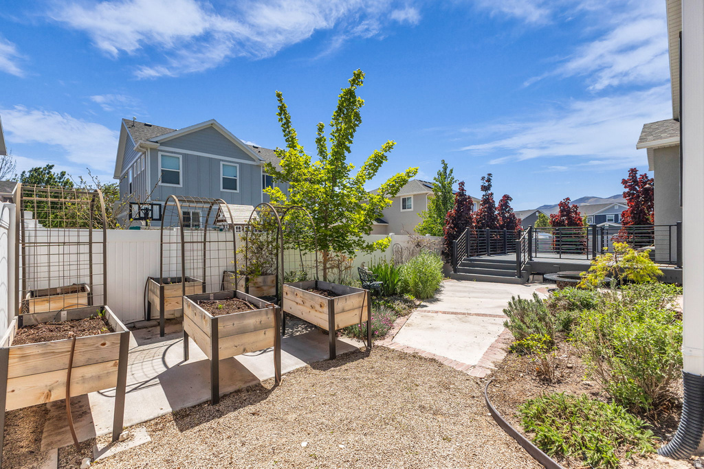 Backyard featuring a multi-level deck with black railings, a gravel yard area, raised garden beds with metal arch trellises, established landscaping, and a privacy fence