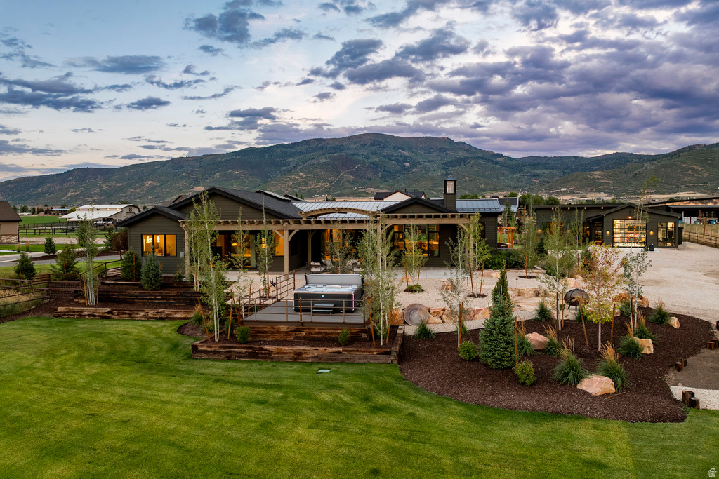Expansive backyard featuring a manicured lawn, tiered landscaping with mature trees and shrubs, a stone patio, and a pergola-covered outdoor space