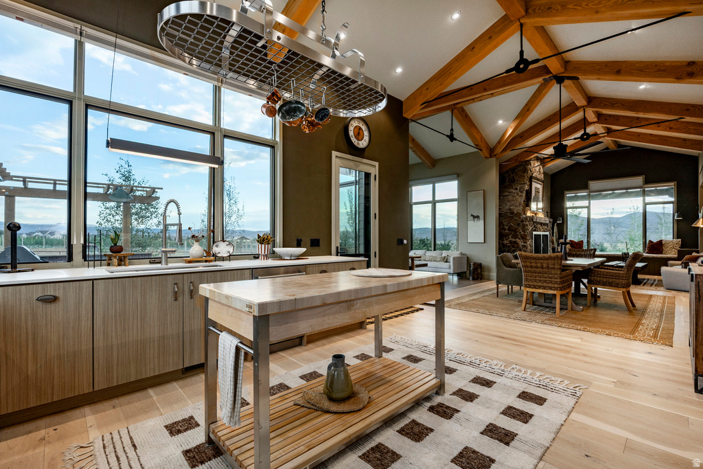 Open-concept kitchen and living area featuring high vaulted ceilings with exposed wood beams, a pot rack, wood-finish flooring, and expansive windows