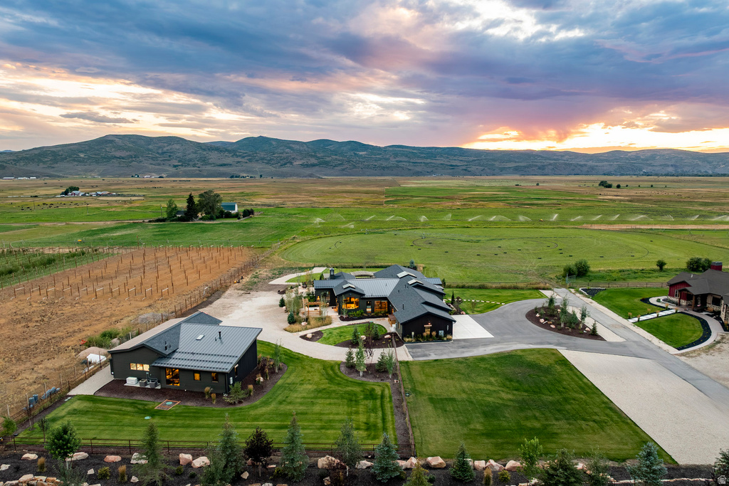 Expansive property featuring two distinct residential structures with dark siding and metal roofs, a circular driveway, manicured lawns, and a cultivated field