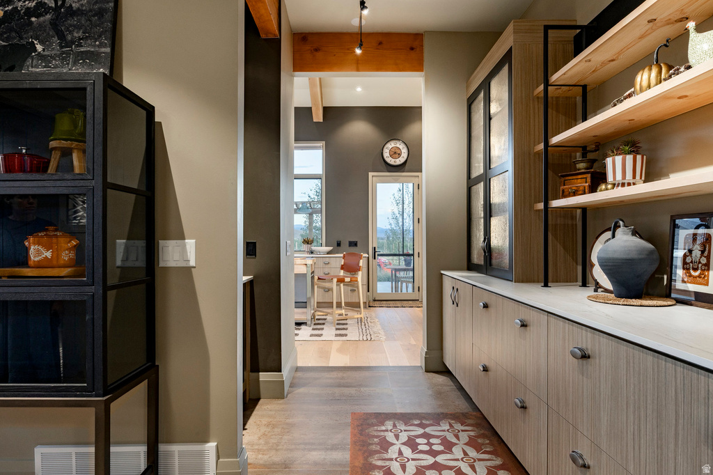 Hallway featuring wood-finish flooring with an accent rug, built-in cabinetry with light wood-finish doors and drawers, a light-toned countertop, and open wood shelving