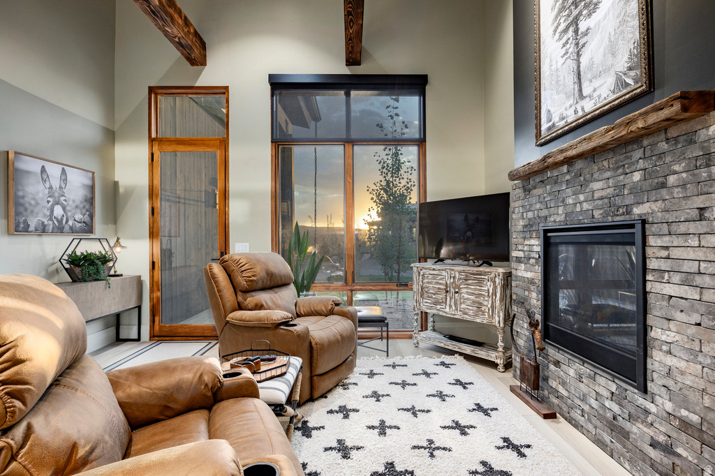 Living area featuring a stone-clad fireplace with a dark metal insert, exposed wood ceiling beams, and high ceilings