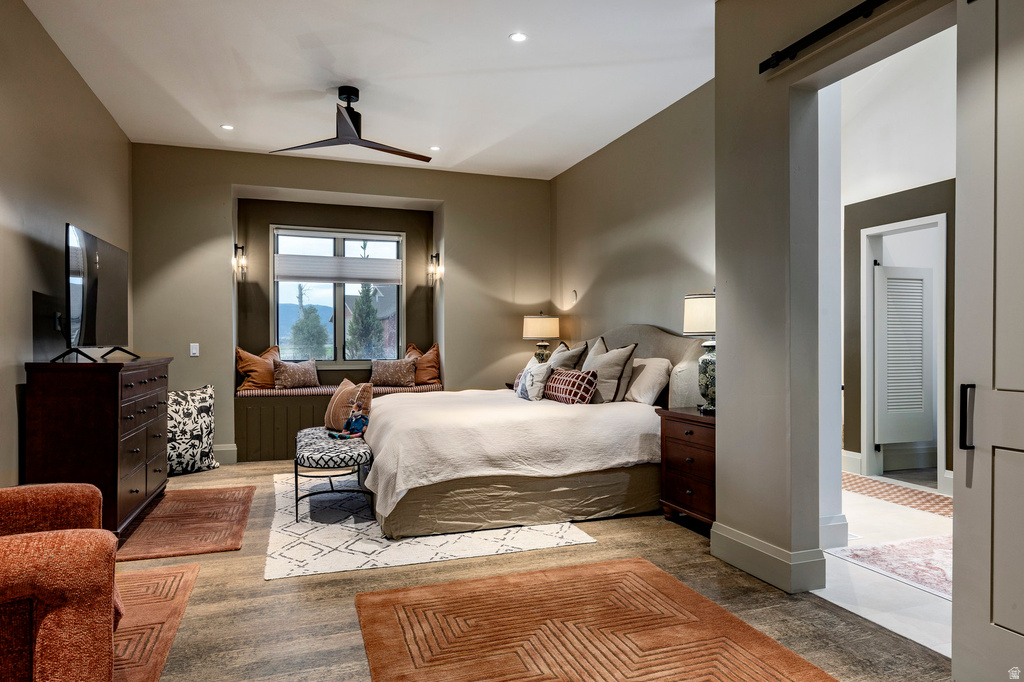 Spacious bedroom featuring wood-finish flooring, a built-in window bench, integrated wall sconces, recessed lighting, and a modern ceiling fan