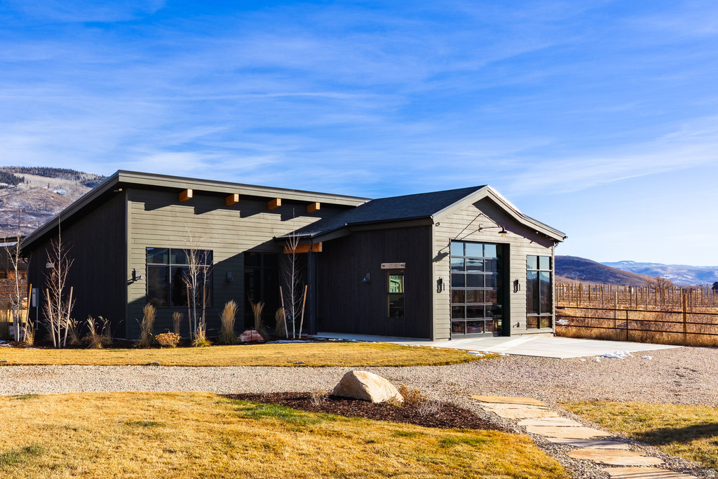 Modern exterior with dark vertical and horizontal siding, exposed wood rafters, a full-view garage door, and a stone paver pathway