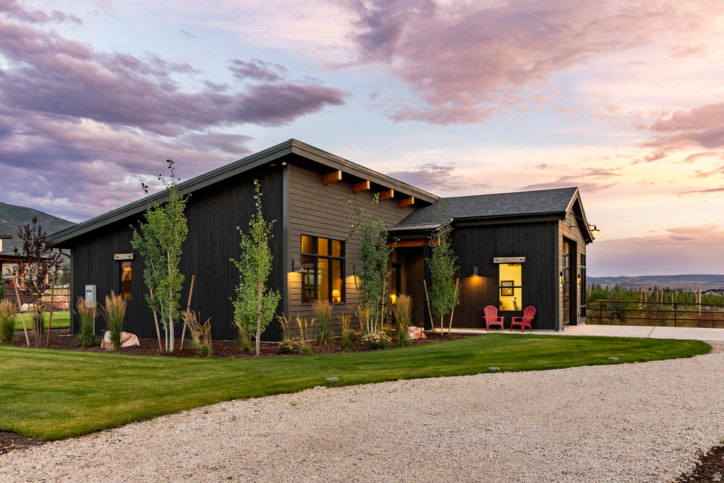 Modern ranch-style residence featuring dark siding, a gravel driveway, and a manicured lawn