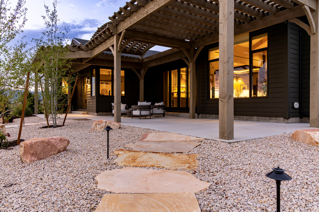 Expansive outdoor living area featuring a wood pergola, concrete patio, and a gravel landscape with large natural stone accents