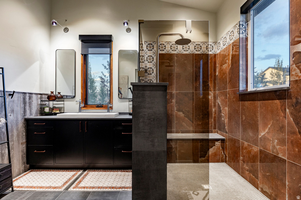 Spacious bathroom featuring a dual vanity with undermount sinks, wood-paneled accent wall, a walk-in shower with a built-in bench, and decorative tiled flooring