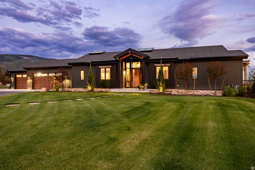 Contemporary residence featuring dark horizontal siding, a prominent front entry with wood accents, and a large three-car garage with wood-paneled doors