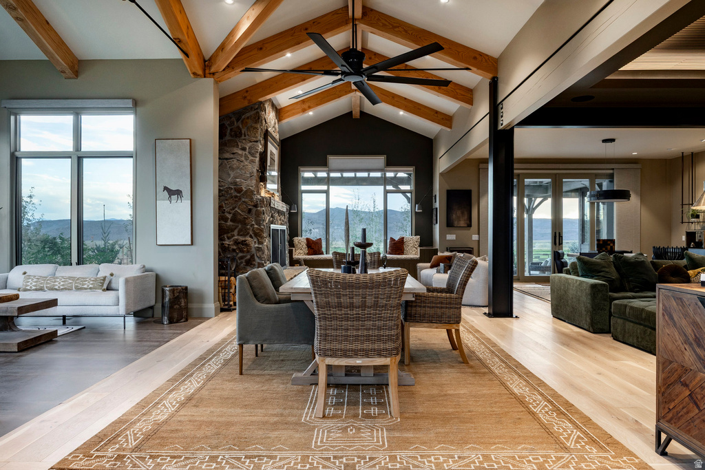 Spacious interior featuring vaulted ceilings with exposed wood beams, a stone fireplace, large windows, light wood-finish flooring, and glass patio doors
