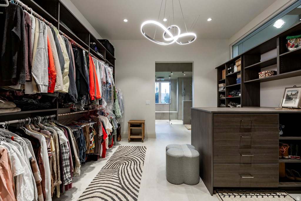 Expansive custom closet featuring extensive dark wood-finish built-in shelving, multiple hanging rods, a central island with integrated drawers, recessed lighting, and a modern linear chandelier