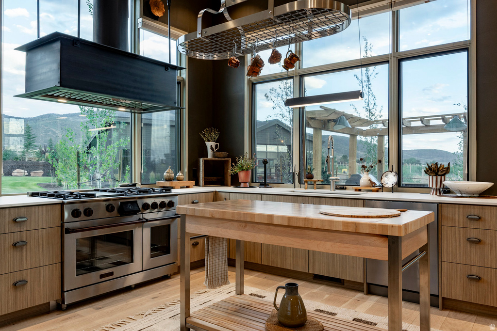 Gourmet kitchen featuring a professional-grade stainless steel range with a custom overhead hood vent, extensive wood-finish cabinetry, light-toned countertops, and large picture windows