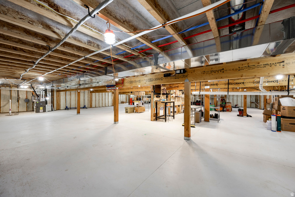 Expansive unfinished basement featuring a concrete floor, exposed wood ceiling joists, visible HVAC ductwork, and dedicated utility area