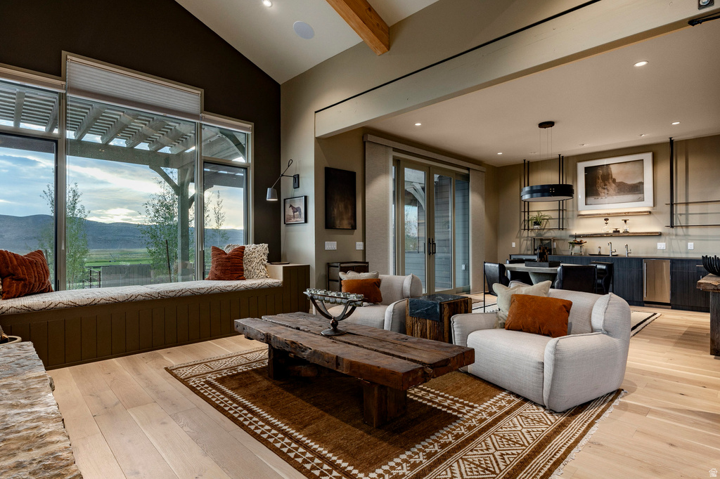 Spacious room featuring a wall of windows with a built-in window seat, wood-finish flooring, exposed ceiling beams, and a wet bar with integrated appliances